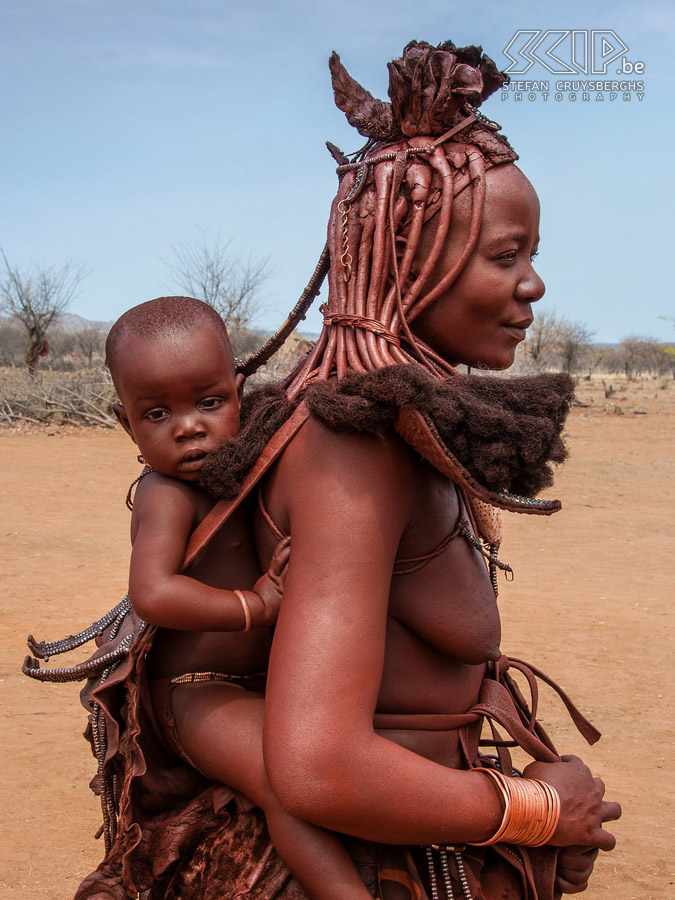 Omangete - Himba vrouw Getrouwde Himba vrouwen dragen hoofdtooien met gevlochten haar en een soort tulband gemaakt van geitenleer en kettingen versierd met schelpen en sieraden gemaakt van ijzer en koper. Ze dragen hun baby's en jonge kinderen op hun rug in een soort lederen rugzak. Stefan Cruysberghs